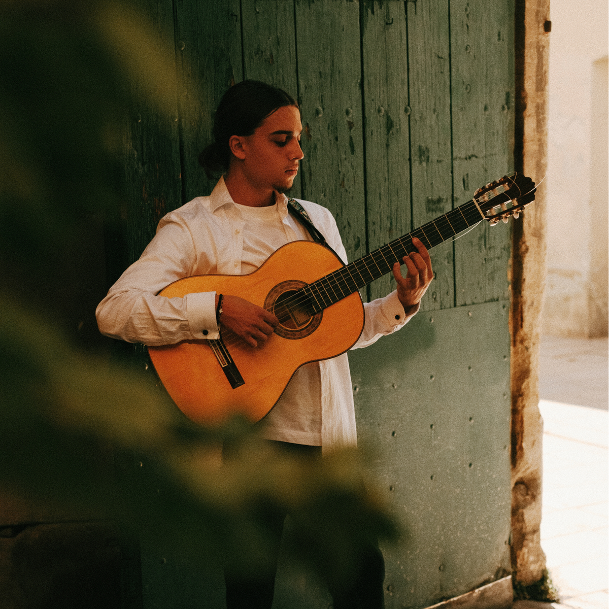 Lucas Fontana joue de la guitare devant une porte ancienne